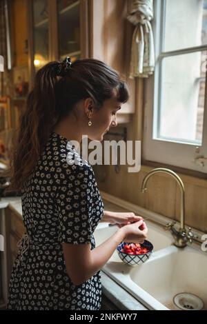 Junge Frau, die Erdbeeren schneidet, steht am Spülbecken Stockfoto