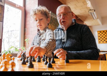 Mein Sohn spielt Schach mit Großvater im Club Stockfoto