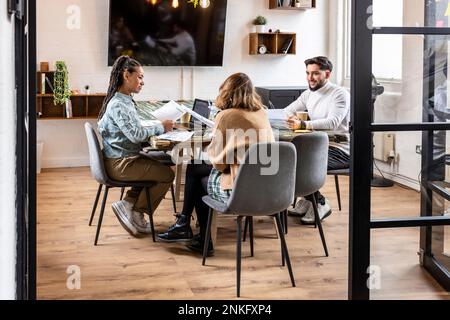 Geschäftskollegen sitzen mit Charts und diskutieren am Tisch im Büro Stockfoto