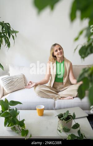 Lächelnde Frau, die zu Hause Yoga auf dem Sofa praktiziert Stockfoto