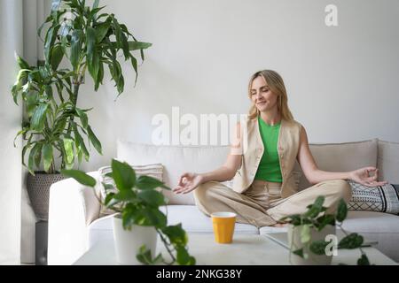 Lächelnde Frau, die zu Hause Meditation auf dem Sofa praktiziert Stockfoto
