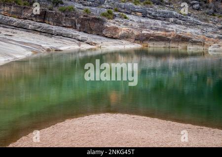 Geologische Granitsteine und Kalksteinwände im Pedernales Falls State Park im Texas Hill Country spiegeln sich in einem grünen Teich Stockfoto