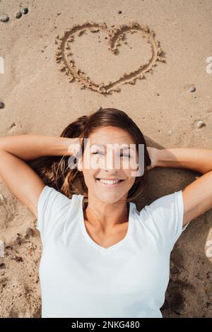 Eine Frau mit Händen hinter dem Kopf, die am Strand ruht Stockfoto