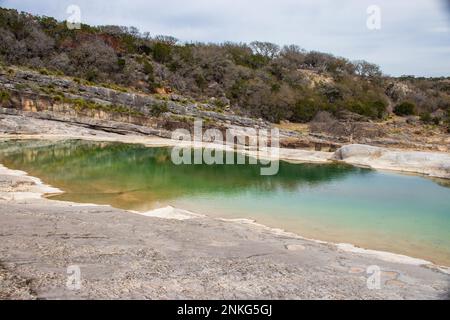 Glatter Kalkstein führt hinunter in den einladenden Pool mit geologischen Felsen im Hintergrund im Pedernales Falls State Park Texas Stockfoto