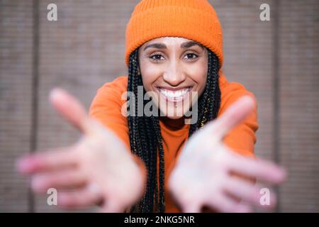 Glückliche Frau mit orangefarbener Strickmütze, die vor der Wand gestrickt wird Stockfoto