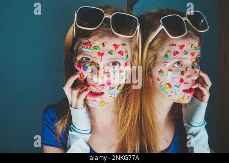 Eine Frau mit Aufklebern über dem Gesicht, die auf blauem Hintergrund in die Finger beißt Stockfoto