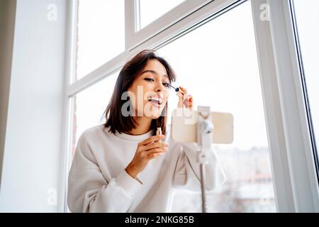 Fröhliche Influencer, die Make-up-Tutorial mit dem Smartphone Filmen Stockfoto