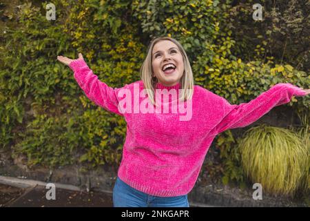 Eine sorgenfreie, reife Frau, die einen rosa Pullover trägt und vor Pflanzen tanzt Stockfoto