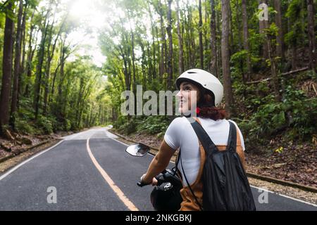 Glückliche Frau mit Helm, die Motorrad auf der Straße fährt Stockfoto