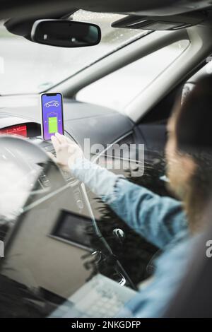 Frau mit Laptop, die die App zum Aufladen eines Elektroautos verwendet, durch Glas gesehen Stockfoto