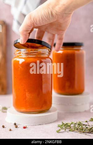 Die Hand einer Frau öffnet den Deckel des Bechers mit Tomatensoße Stockfoto