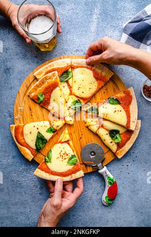 Hände halten Pizza und ein Glas Bier auf dem Tisch auf der Party Stockfoto