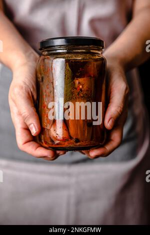 Die Hände einer reifen Frau in der Hand, die selbstgemachte eingelegte Auberginen-Gläser hält Stockfoto