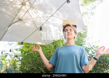 Eine Frau, die Bücher auf dem Kopf im Garten ausbalanciert Stockfoto
