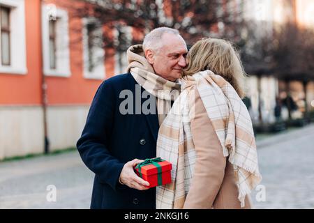 Ein älterer Mann mit Geschenkbox, der mit einer Frau auf der Straße steht Stockfoto