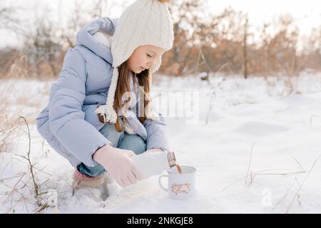 Ein Mädchen mit Strickmütze, das heiße Schokolade in den Becher schüttet Stockfoto