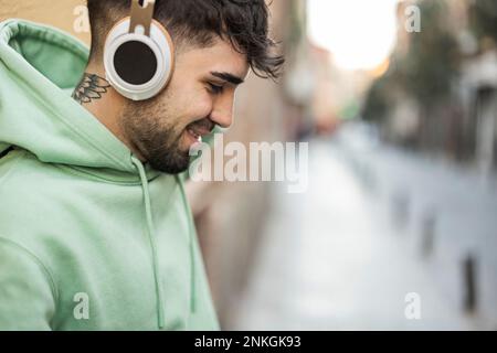 Lächelnder Mann mit Kopfhörern, der Musik auf dem Fußweg hört Stockfoto