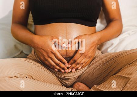 Schwangere Frau, die mit den Händen am Bauch Herzform bekommt Stockfoto