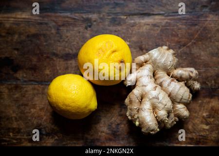 Zwei frische Zitronen und Ingwerwurzel liegen auf einer Holzfläche Stockfoto