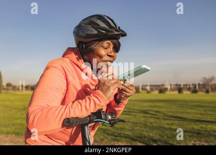 Glückliche Seniorin auf dem Roller, die an sonnigen Tagen mit Freisprechtelefon telefoniert Stockfoto