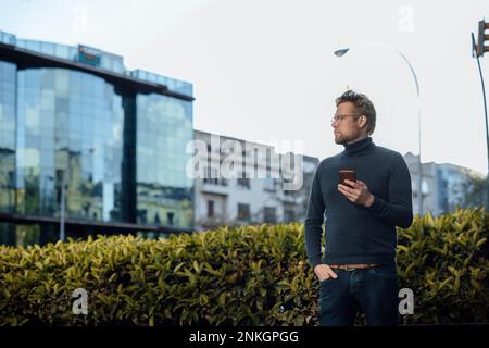 Mann, der ein Handy hält, mit der Hand in der Tasche Stockfoto