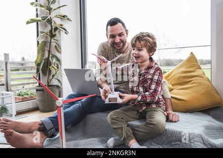 Süßer Sohn, der mit einem Windturbinenmodell spielt, vom Vater, der zu Hause sitzt Stockfoto