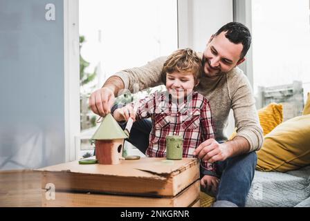Glücklicher Vater und Sohn, der zu Hause ein Modellhaus malt Stockfoto