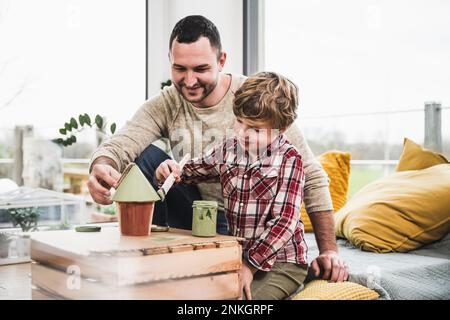 Lächelnder Sohn malt Modellhaus von Vater zu Hause Stockfoto