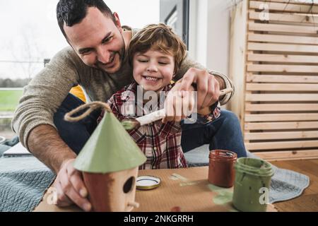 Glücklicher Vater und Sohn, die zusammen zu Hause ein Modellhaus malen Stockfoto