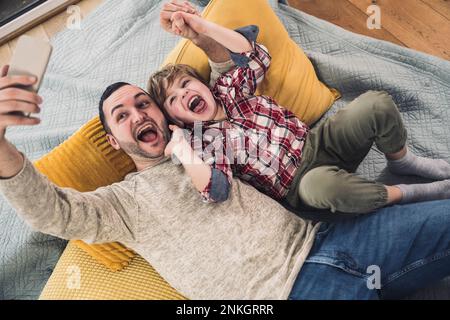 Fröhlicher Sohn mit Vater, der zu Hause Selfie über Smartphone macht Stockfoto