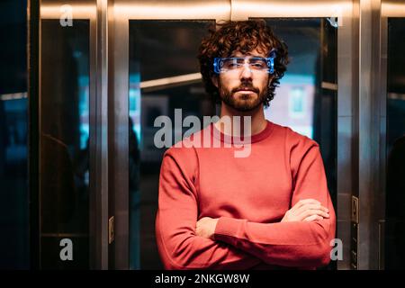 Junger Mann mit kluger Brille und gekreuzten Armen im Aufzug Stockfoto