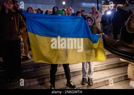 London, Großbritannien. 23. Februar 2023. Während der Kundgebung am Trafalgar Square sehen Sie kleine Kinder, die zusammen eine ukrainische Flagge halten. DIE US-Botschaft London und die Botschaft der Ukraine in Großbritannien haben sich am Vorabend des 1.-jährigen Bestehens des Russisch-Ukraine-Krieges gemeinsam an einer Kundgebung am Trafalgar Square in London mit der Ukraine beteiligt. Kredit: SOPA Images Limited/Alamy Live News Stockfoto