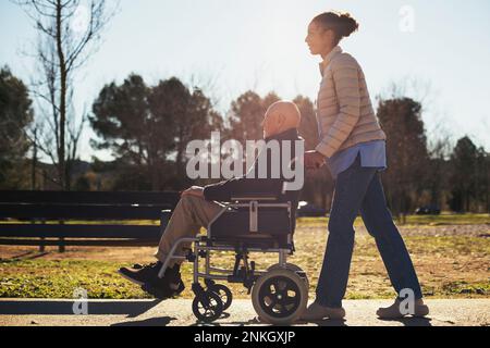 Hausmeister schubst Senior Mann im Rollstuhl im Park Stockfoto