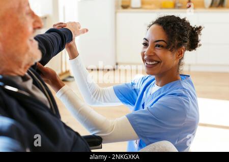 Fröhliche Krankenschwester, die Seniorenhelfer beim Sport zu Hause unterstützt Stockfoto