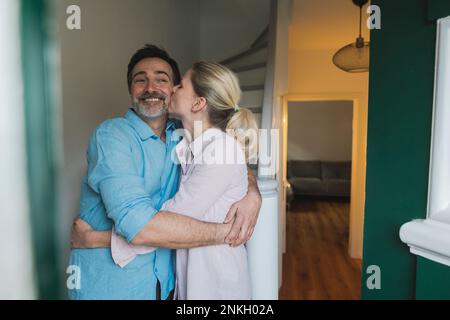 Reife Frau, die ihren Ehemann zu Hause küsst und umarmt Stockfoto