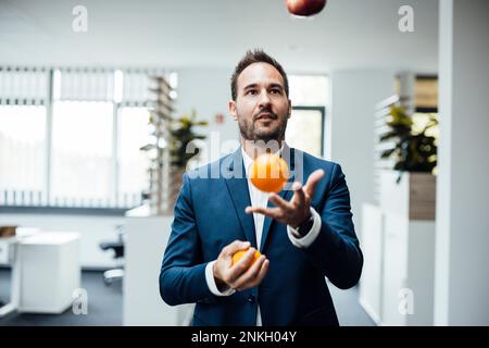 Geschäftsmann jongliert im Büro mit Orangen Stockfoto