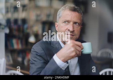 Rücksichtsvoller, reifer Geschäftsmann mit Kaffeetasse durch Glas gesehen Stockfoto