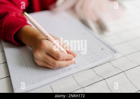 Die Hände eines Mädchens, das zu Hause Mathe-Hausaufgaben macht Stockfoto