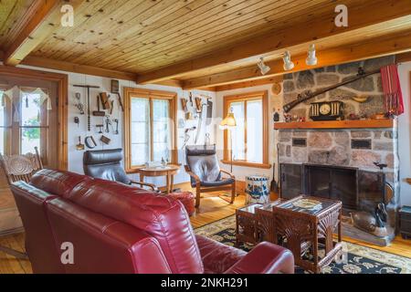 Burgunder Ledersofa mit Holz und braunen Ledersesseln und 3-teiligem Korbglas-Bambus-Kaffeetisch im Wohnzimmer im alten Haus aus dem Jahre 1840. Stockfoto