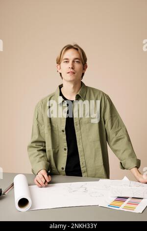 Junger Modedesigner mit Skizze am Schreibtisch im Studio Stockfoto