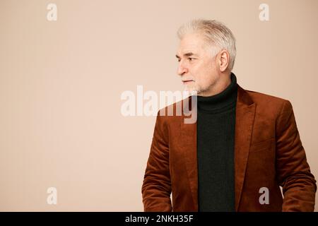 Hübscher, reifer Mann mit Blazer vor beigefarbenem Hintergrund Stockfoto
