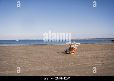 Ältere Frau, die sich am sonnigen Tag entspannt und auf das Meer blickt Stockfoto