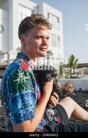Ein junger Mann sitzt mit einem süßen Hund im Vorgarten Stockfoto
