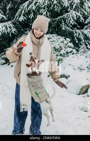 Lächelnde junge Frau, die mit dem Hund im Schneepark spielt Stockfoto