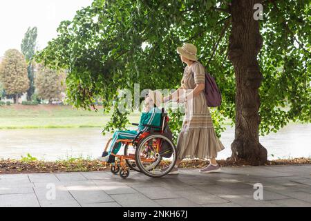 Mutter schubst Tochter im Rollstuhl auf dem Fußweg Stockfoto