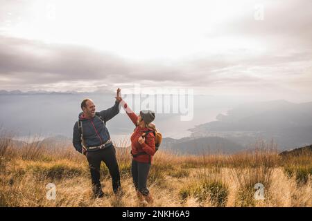 Fröhlicher Mann und Frau, die sich gegenseitig High Five geben, wenn sie auf dem Berg stehen Stockfoto