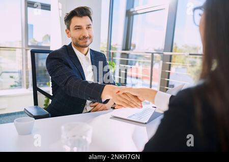 Ein lächelnder Rekrutierer, der mit dem Kandidaten im Amt die Hand schüttelt Stockfoto