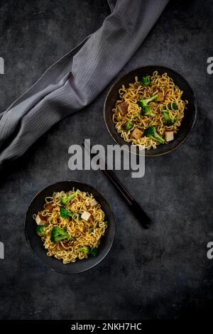 Studiofoto mit zwei Tellern verzehrfertiger veganer Nudeln mit Brokkoli, Tofu und Sojasoße Stockfoto