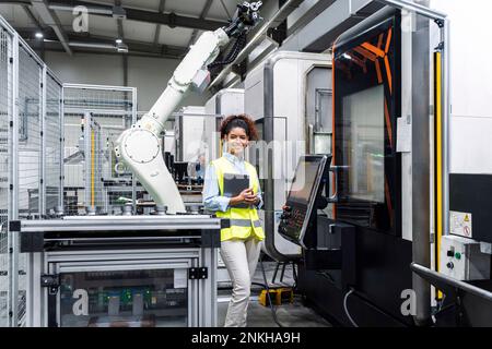 Lächelnder Ingenieur, der in der Fabrik mit Tablet-Computer für Maschine steht Stockfoto