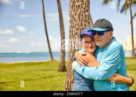 Seniorenpaar umarmt sich im Park in der Nähe eines Strandes Stockfoto
